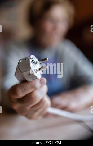 Personne âgée tenant un câble d'alimentation avec prise dans la main à la maison, symbolisant les coûts de l'énergie et la pauvreté, Cologne, Rhénanie du Nord-Westphalie, Allemagne Banque D'Images