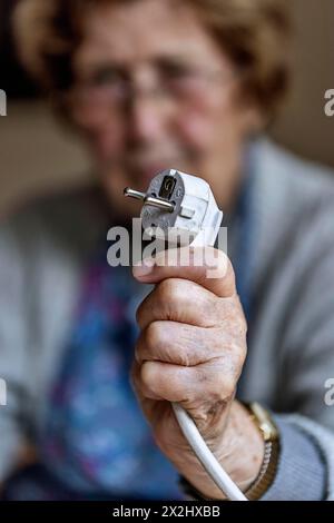 Personne âgée tenant un câble d'alimentation avec prise dans la main à la maison, symbolisant les coûts de l'énergie et la pauvreté, Cologne, Rhénanie du Nord-Westphalie, Allemagne Banque D'Images