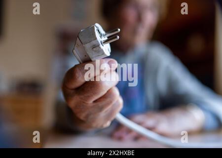 Personne âgée tenant un câble d'alimentation avec prise dans la main à la maison, symbolisant les coûts de l'énergie et la pauvreté, Cologne, Rhénanie du Nord-Westphalie, Allemagne Banque D'Images