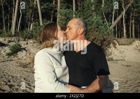 Un homme et une femme s'embrassant romantiquement sur la plage de sable avec les vagues de l'océan en arrière-plan. Banque D'Images