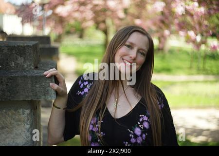 Portrait d'une femme entourée par les branches d'un cerisier ornemental orné de délicates fleurs de cerisier roses et de feuilles vert-jaune luxuriantes. S Banque D'Images