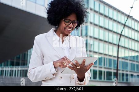 Agent immobilier féminin africain mature joyeux utilisant la tablette pour envoyer des messages en ligne pour le travail. Banque D'Images