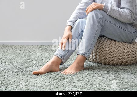 Femme pieds nus assise sur un pouf et un tapis moelleux vert près du mur léger Banque D'Images