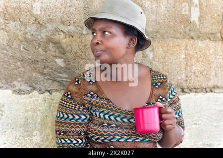 jeune femme africaine chubby avec un chapeau tenant une tasse dans le township pauvre, colonie informelle Banque D'Images