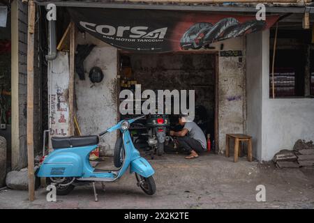 Dans un garage urbain rustique, un mécanicien se concentre sur la réparation d'une moto. Un scooter vintage est placé en évidence au premier plan, suggérant un bus Banque D'Images