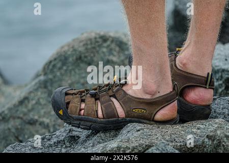 Vue détaillée d'une paire de sandales d'extérieur durables portées par une personne debout sur un sol rugueux et rocheux. La chaussure présente une conception robuste adaptée à Banque D'Images
