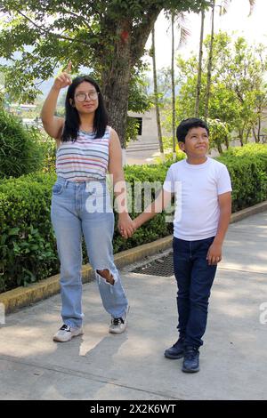 Sa sœur de 16 ans s’occupe de son frère latino de 10 ans, à la peau foncée, seule dans le parc, sans les soins de ses parents Banque D'Images