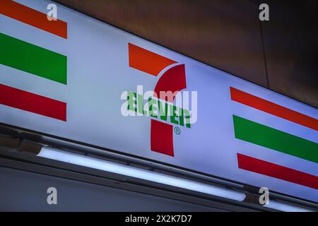 Une image en gros plan de l'enseigne du magasin 7-Eleven, avec leur logo emblématique avec des bandes rouges, vertes et oranges soulignées par un éclairage doux. Banque D'Images