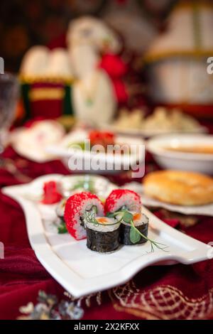 Une variété de rouleaux de sushi, ainsi que d'autres plats variés, sont disposés sur une table avec une nappe rouge. Banque D'Images