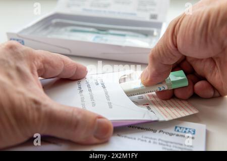 Londres. UK- 04.17.2024. Une personne mettant l'échantillon de cancer de l'intestin recueilli dans l'enveloppe pour être envoyé à des fins de test. Banque D'Images