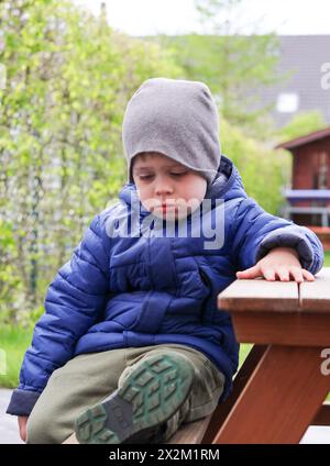Un mignon petit garçon en bas âge assis triste sur un banc à l'extérieur à Hone Banque D'Images