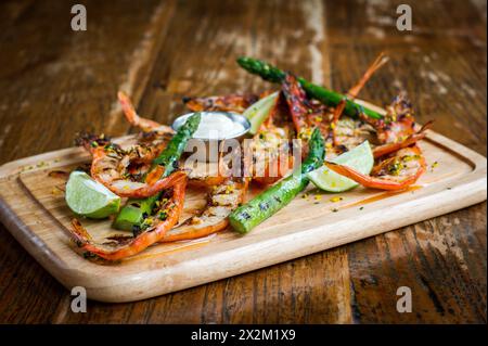 Crevettes grillées avec citron vert, asperges et mayonnaise sur planche de bois dans un restaurant Banque D'Images