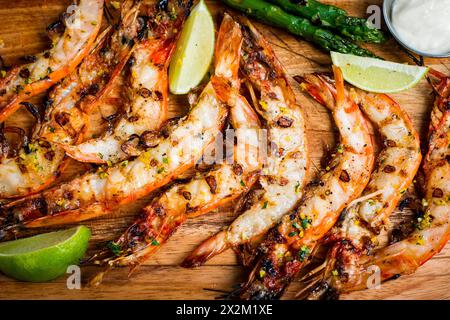 Vue de dessus gros plan de crevettes grillées avec citrons verts, asperges et mayonnaise sur planche de bois Banque D'Images