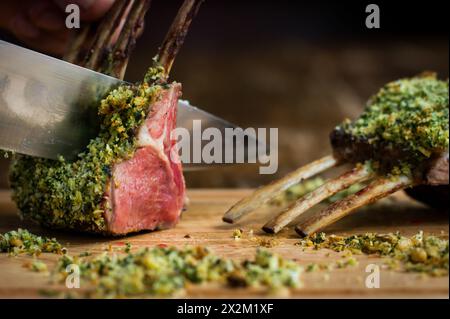 Rack d'agneau avec croûte d'herbes de noisette coupé avec un grand couteau sur planche de bois dans le restaurant Banque D'Images