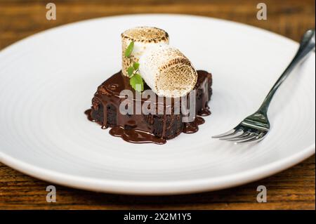 Brownie avec sauce chocolat et s'mores sur assiette blanche avec fourchette sur table de restaurant en bois Banque D'Images