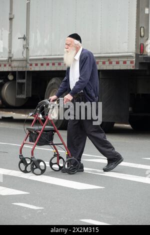 Un homme juif hassidique plus âgé traversant une rue tout en poussant un marcheur. À Brooklyn, New York, 2024. Banque D'Images