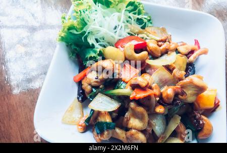 Cuisine thaïlandaise, poulet sauté avec des noix de cajou sur une assiette blanche, assiette de nourriture sur une table en bois avec lumière naturelle de la fenêtre. Banque D'Images