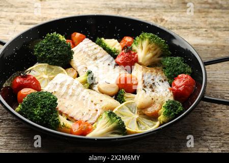 Morue savoureuse cuite avec des légumes dans une poêle à frire sur une table en bois, gros plan Banque D'Images