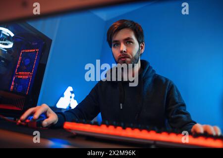 Portrait de jeune joueur professionnel jouant en ligne sur son PC moderne. Il est sérieux et concentré sur le jeu, ayant un tournoi d'esport, jouant dans un jeu vidéo multijoueur à la maison. Jeu de tir à la première personne Banque D'Images
