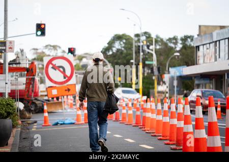 Homme marchant sur la route avec des cônes orange détournant la circulation. Arrêt de bus bloqué par les cônes de circulation. Travaux routiers à Auckland. Banque D'Images