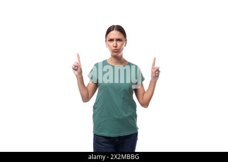 jeune femme aux cheveux noirs dans un t-shirt de base vert avec surprise raconte la nouvelle Banque D'Images