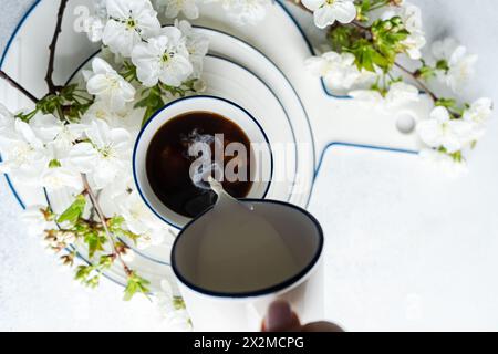 Crème versée dans une tasse de café, entourée de fleurs de cerisier blanc Banque D'Images