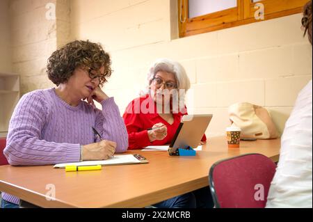 Deux femmes âgées axées sur l'apprentissage, engagées dans une session d'étude de groupe avec tablette numérique et notes Banque D'Images