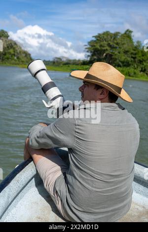 Homme portant un chapeau dans un bateau prenant des photos avec un appareil photo dans une rivière Banque D'Images