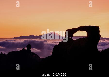 Les couleurs captivantes du coucher de soleil baignent les silhouettes du Roque Nublo et du Mont Teide, avec une mer de nuages flottant sous Gran Canaria Banque D'Images