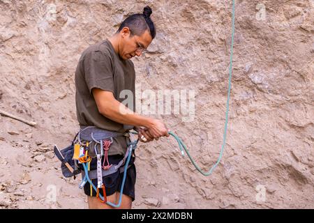 Un grimpeur attentif vérifie sa corde et son équipement sur un fond rocheux, soulignant la sécurité dans les sports d'escalade Banque D'Images