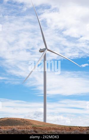 Une éolienne solitaire se dresse contre un ciel bleu nuageux sur une colline aride, symbolisant l'énergie durable Banque D'Images