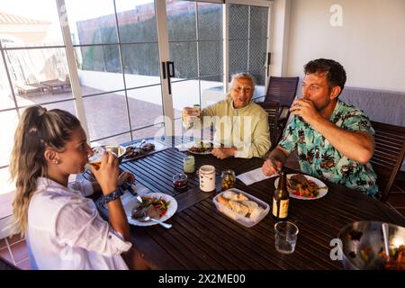 Une famille profite d'un repas barbecue sur un patio extérieur avec une femme âgée et un chien présent, partageant un moment de convivialité. Banque D'Images