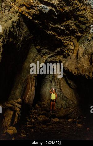 Femme avec une lampe frontale explore la vaste obscurité d'une grotte souterraine naturelle, mettant en évidence les textures rocheuses autour. Banque D'Images