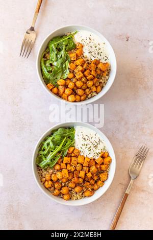 Deux bols de salade de quinoa nappés de patates douces rôties et de pois chiches épicés servis avec une cuillère de sauce yaourt Banque D'Images