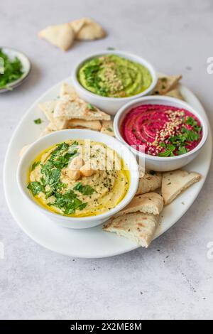 Une exposition vibrante de trois variations de houmous différentes, classique, betterave et avocat, chacune garnie d'herbes fraîches et servie avec du pain pita. Banque D'Images