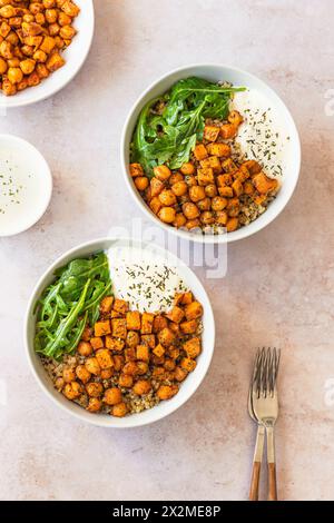 Deux bols de salade de quinoa nutritive garnie de pois chiches épicés, de cubes de patates douces rôties, de roquette fraîche et d'une cuillère de sauce crémeuse au yogourt, gar Banque D'Images