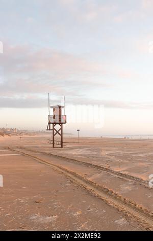 Une tour vide de sauveteur se dresse sur une plage tranquille avec un ciel pastel doux au crépuscule, soulignant l'atmosphère paisible hors saison. Banque D'Images