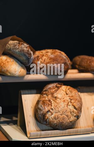 Pain au levain artisanal fraîchement cuit, exposé sur des étagères en bois, mettant en valeur l'extérieur croustillant et la texture artisanale. Banque D'Images