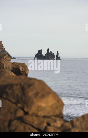 Une vue sereine sur les célèbres piles de mer de Reynisdrangar émergeant de l'océan Atlantique Nord, comme vu depuis les plages de sable noir près de Vik, en Islande Banque D'Images