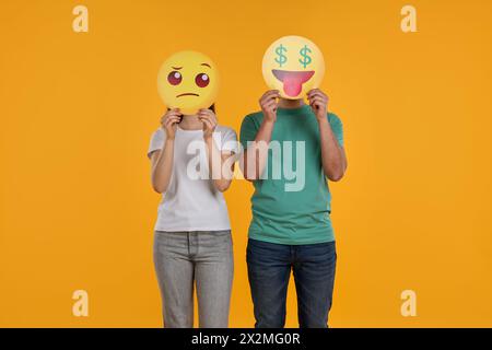 Personnes couvrant les visages avec des émoticônes sur fond jaune Banque D'Images