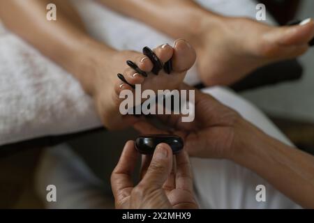 Gros plan d'une femme recevant un massage aux pierres chaudes dans un salon de spa Banque D'Images