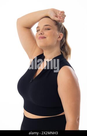 Modèle féminin caucasien de taille plus étire le bras derrière la tête sur fond blanc Banque D'Images