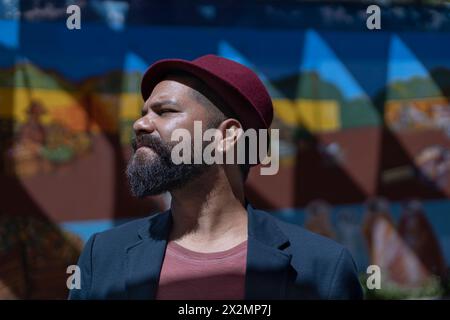 Portrait d'homme bohème latino-américain de profil avec barbe, chapeau et veste. Fond de mur coloré. Concept de vraies personnes Banque D'Images