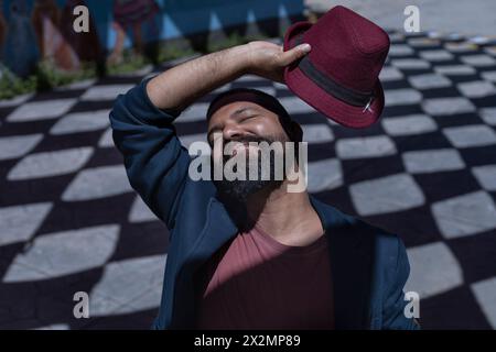 Portrait d'homme bohème latino-américain avec les yeux fermés, barbe, chapeau et veste. Fond d'ombres avec des formes de losange. Concept de vraies personnes. Banque D'Images