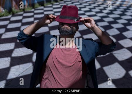 Portrait d'homme bohème d'Amérique latine avec barbe, chapeau et veste. Il porte son chapeau d'une façon drôle cachant son visage. Arrière-plan des ombres avec R Banque D'Images