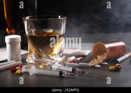 Alcoolisme et toxicomanie. Whisky en verre, seringues, pilules et cigarettes sur table grise Banque D'Images