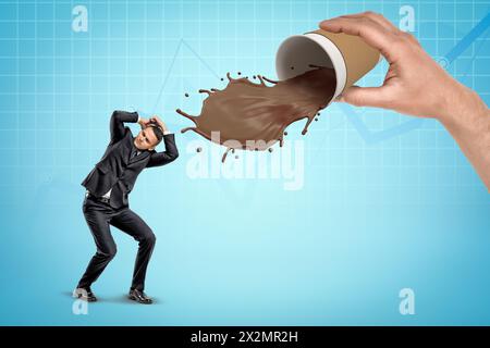 Homme d'affaires se protégeant avec les mains du café renversant hors de la tasse de café en papier dans la main de l'homme sur fond bleu Banque D'Images