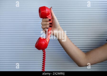 Combiné rouge tenu par la main d'une femme. Fond gris. Concept de technologie vintage. Banque D'Images