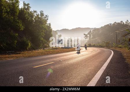 Moto conduite sur la route asphaltée dans le paysage rural au lever du soleil. Route de campagne avec belle route au milieu de la belle forêt de montagne dans Un Banque D'Images