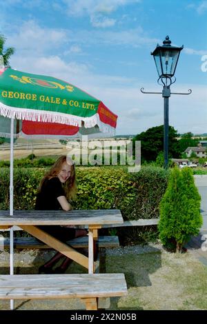 jeune femme blonde jolie naturelle souriante assise dans le jardin au pub rouge du lion chalton hampshire angleterre des années 1990 Banque D'Images